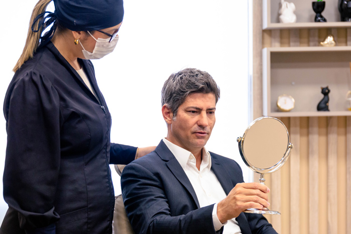 Homem em consultório com profissional da estética, olhando resultados da estética masculina em espelho.