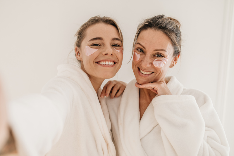 Duas mulheres com roupão e adesivo de skincare no rosto.