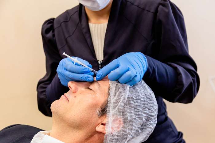 Profissional realizando harmonização facial masculina em paciente maduro.