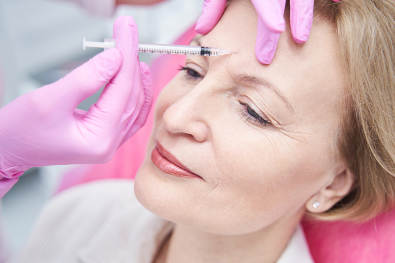 Mulher fazendo aplicação de botox nas rugas entre as sobrancelhas.