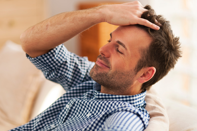 homem passando a mão no cabelo com expressão de satisfação com o cabelo sem calvíce ou queda